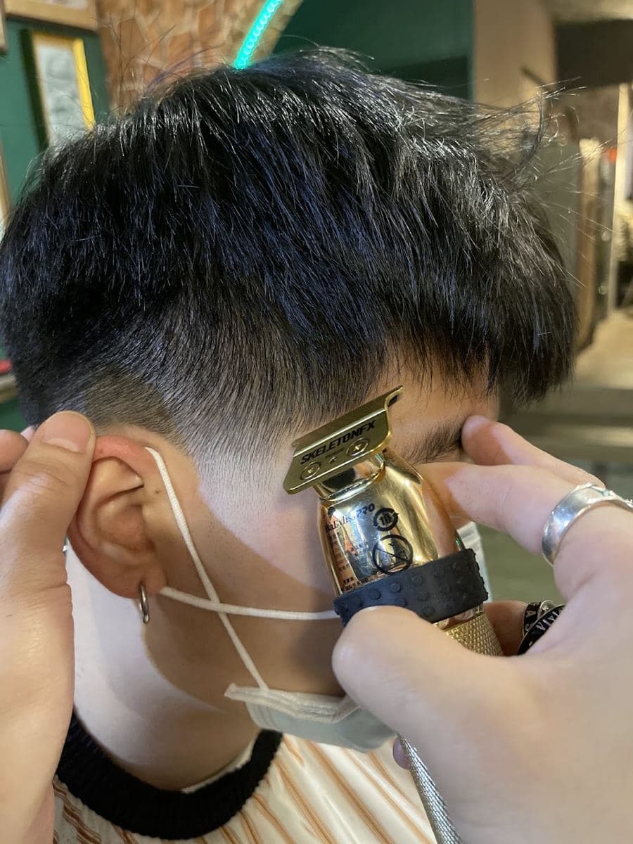 理髮師用電剪修整鬢角與側邊的特寫,頂部頭髮留有長度並往前帶出瀏海